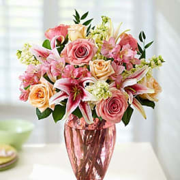 Pink and peach roses with lilies in a pink glass vase