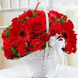 Red roses and gerbera daisies in a white basket with a ribbon