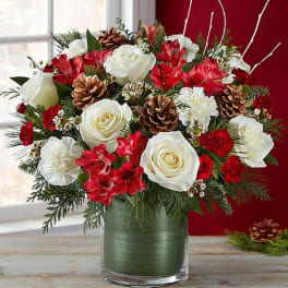 Red and white floral arrangement in a glass vase with pinecones
