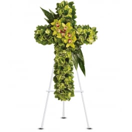 Green floral cross standing spray with yellow-green orchids on a white easel.