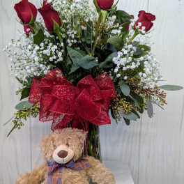 Red roses in a vase with a teddy bear in front