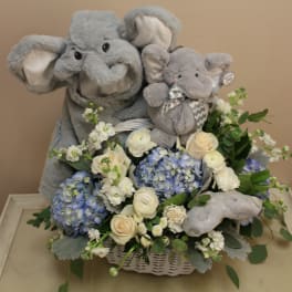 Two gray plush elephants in a basket with blue and white flowers