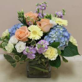 Mixed bouquet of roses, hydrangeas, and daisies in a square glass vase