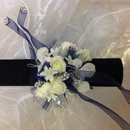 White floral wrist corsage with blue ribbon on a black band