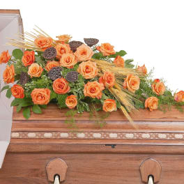 Orange rose casket spray with wheat accents arranged on a wooden casket