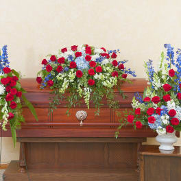 Red, white, and blue funeral floral set with casket spray and side arrangements on a wooden casket