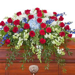Red, white, and blue casket spray with roses, carnations, and mixed flowers on a wooden casket