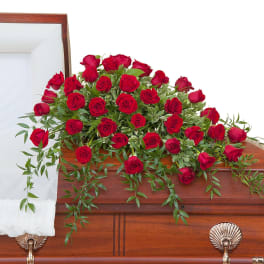 Red rose casket spray arranged across a polished wooden casket.
