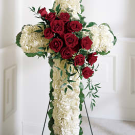 Red roses arranged on a white floral cross with a stand
