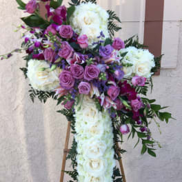 Cross-shaped floral tribute with white roses and purple flowers on an easel