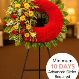 Standing red wreath with yellow and red flowers on one side, displayed on a black easel indoors