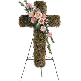 Moss-covered cross with pink and peach flowers on a stand
