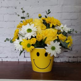 Yellow and white flower arrangement in a smiley-face pot