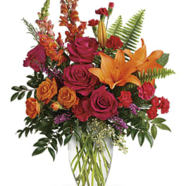 Bright bouquet of orange lilies and pink roses in a clear glass vase