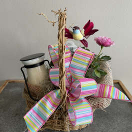 Basket arrangement with a pink flower, bird ornament, and striped ribbon