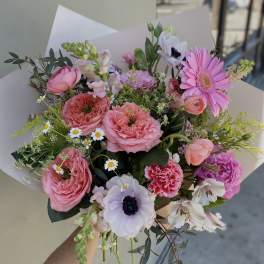 Handheld bouquet of pink and white mixed flowers wrapped in paper