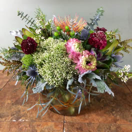 Mixed floral arrangement in a low glass vase with pink and burgundy blooms