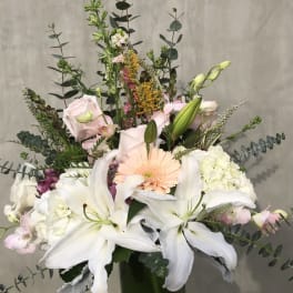 Tall bouquet of white lilies, pale pink roses, and a peach gerbera in a glass vase
