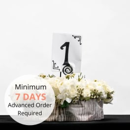 Low white floral centerpiece in a round container with a table number one sign.