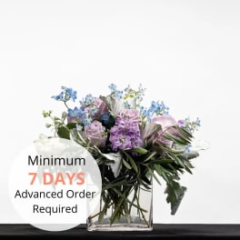 Lavender and blue flower arrangement with silver foliage in a clear glass cube vase