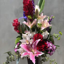 Tall bouquet of red roses, pink lilies, and orchids in a black vase
