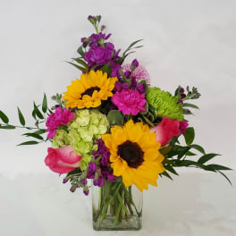 Mixed bouquet with sunflowers, roses, and purple blooms in a clear glass vase