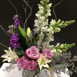 Mixed bouquet of pink roses, white lilies, and purple snapdragons in a glass vase