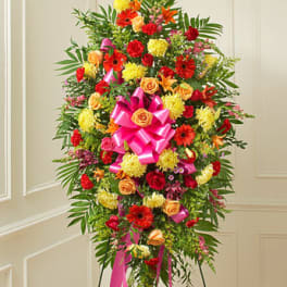Tall standing floral spray with red, yellow, and orange flowers and pink ribbon
