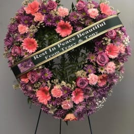 Heart-shaped funeral wreath with pink and purple flowers on a stand