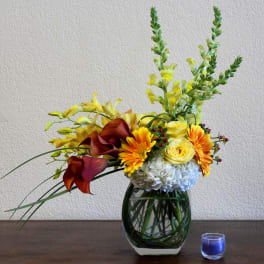 Yellow and orange floral arrangement in a glass vase with a blue candle nearby