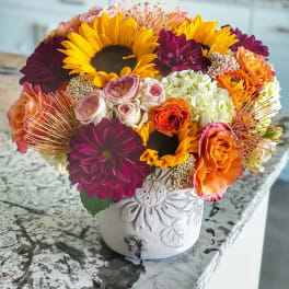 Bright mixed bouquet with sunflowers, dahlias, and roses in a white vase
