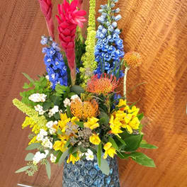 Tall mixed bouquet in a textured glass vase with pink, blue, yellow, and orange flowers