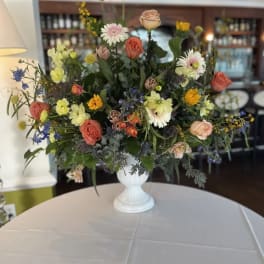Mixed floral arrangement in a white pedestal vase with roses and daisies