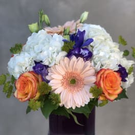 Mixed bouquet with hydrangeas, roses, and a gerbera daisy in a dark vase