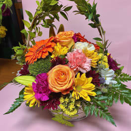 Colorful mixed flower basket with roses, daisies, and carnations under a leafy arch