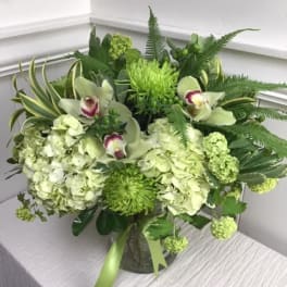 Green floral arrangement with orchids and hydrangeas in a glass vase