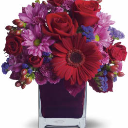 Red roses and purple daisies arranged in a clear square vase
