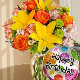 Bouquet of yellow lilies, orange roses, and pink alstroemeria with a birthday balloon