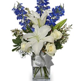 White lilies and roses in a clear glass vase with blue flowers