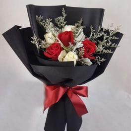 Bouquet of red and white roses wrapped in black paper with a red ribbon