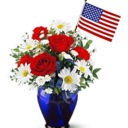 Red roses and white daisies in a blue vase with a small American flag