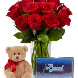 Red roses in a glass vase with a teddy bear and boxed chocolates