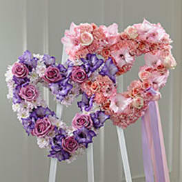 Two heart-shaped floral arrangements on stands in pink and purple.
