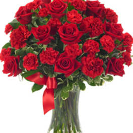 Red roses and carnations in a clear glass vase with a red ribbon