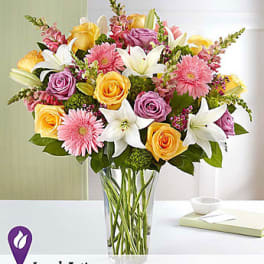 Mixed bouquet of roses, lilies, and pink daisies in a clear glass vase