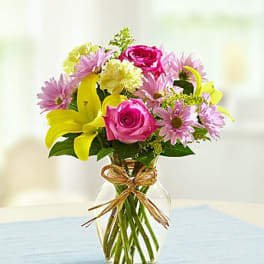 Pink roses and yellow lilies in a glass vase with a ribbon