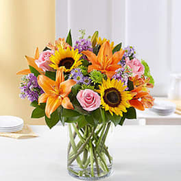 Mixed bouquet of sunflowers, orange lilies, and pink roses in a glass vase
