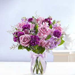 Pink and purple bouquet in a clear glass vase with a lavender ribbon