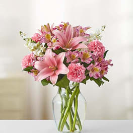 Pink lilies and carnations arranged in a clear glass vase