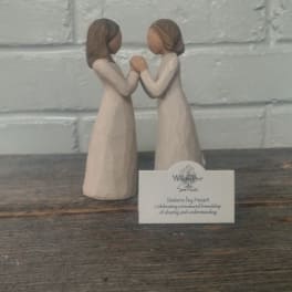 Two small figurines of girls facing each other and holding hands